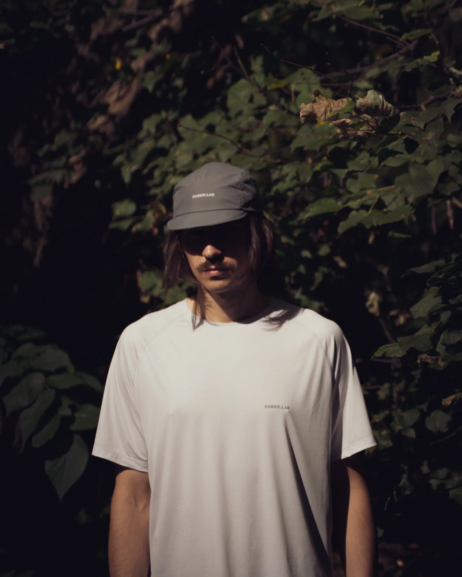 Biegacz w szarej czapce 5 Panels Cap i jasnej koszulce na tle zieleni