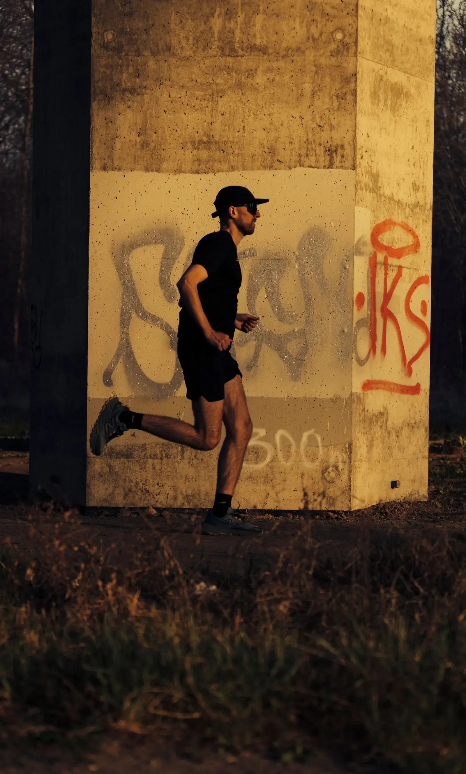 Michał biegnie przy betonowym filarze z graffiti